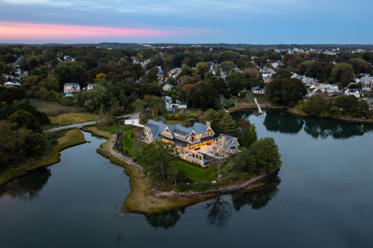 Aerial twilight view of a custom luxury waterfront home on a peninsula in Beverly MA, with stone chimney by Victor & Sons Masonry Photo by Matt McNamara.