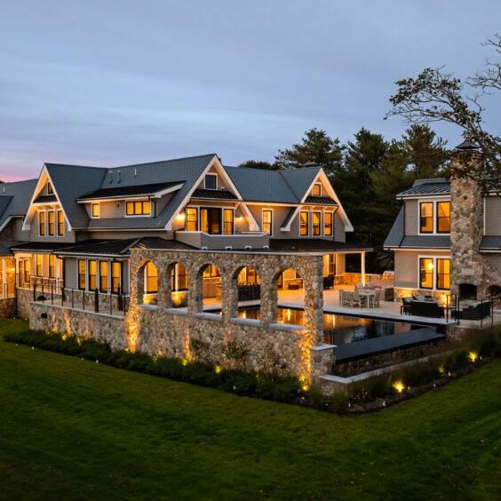 Stoneyard Kems Beverly | Exterior | Rear Pool Stone Chimney Rear elevation at dusk with pool and stone chimney clad in Stoneyard Boston Blend Round 140 by Victor & Sons Masonry Photo by Matt McNamara.
