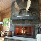Monadnock Square Rectangular stone veneer fireplace with active fire, dark quartzite tones complementing log cabin interior.