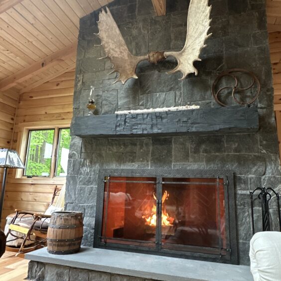 Monadnock Square Rectangular Fireplace D Paoletti 02 Monadnock Square Rectangular stone veneer fireplace with active fire, dark quartzite tones complementing log cabin interior.