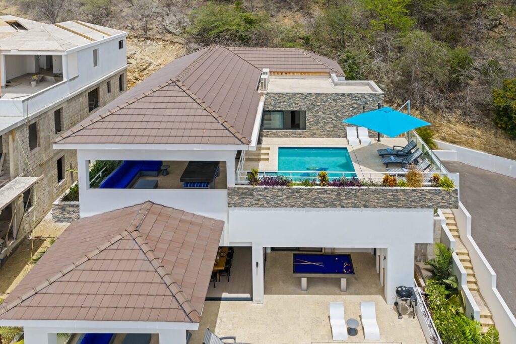 Overhead drone view of a villa with a rooftop pool bordered by stacked stone parapet walls.