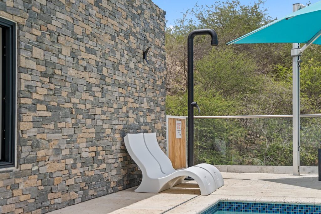 Close-up of a stacked ledgestone wall in gray, beige and rust tones beside a white lounge chair and outdoor shower.