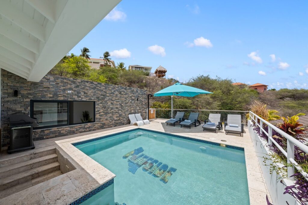 Rooftop pool with the Cliffside logo in the tile, next to a long stacked stone wall under a blue sky.