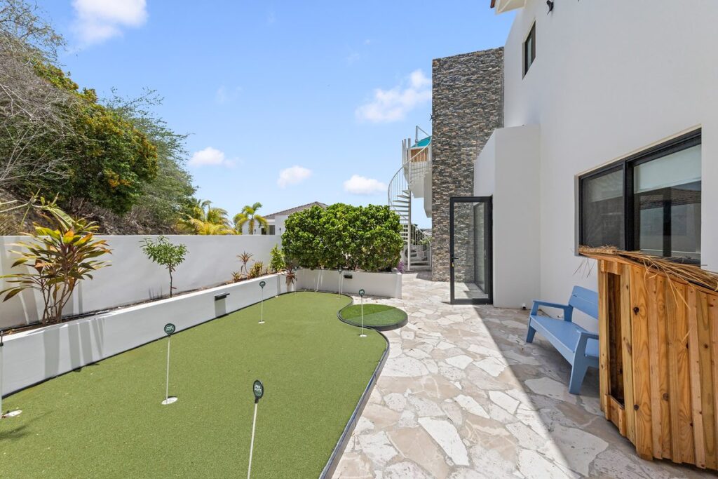 Backyard putting green and flagstone path beside a white house with a tall stacked stone tower.