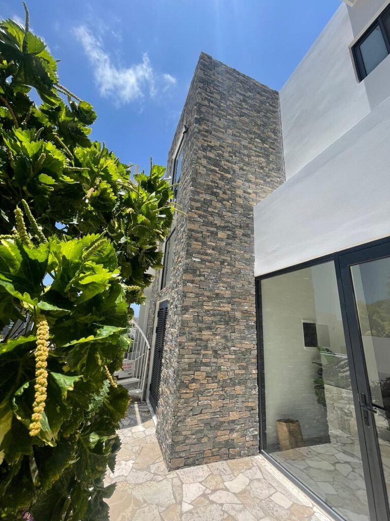 Stacked stone column next to a glass door and white wall, with tropical leaves in the foreground.
